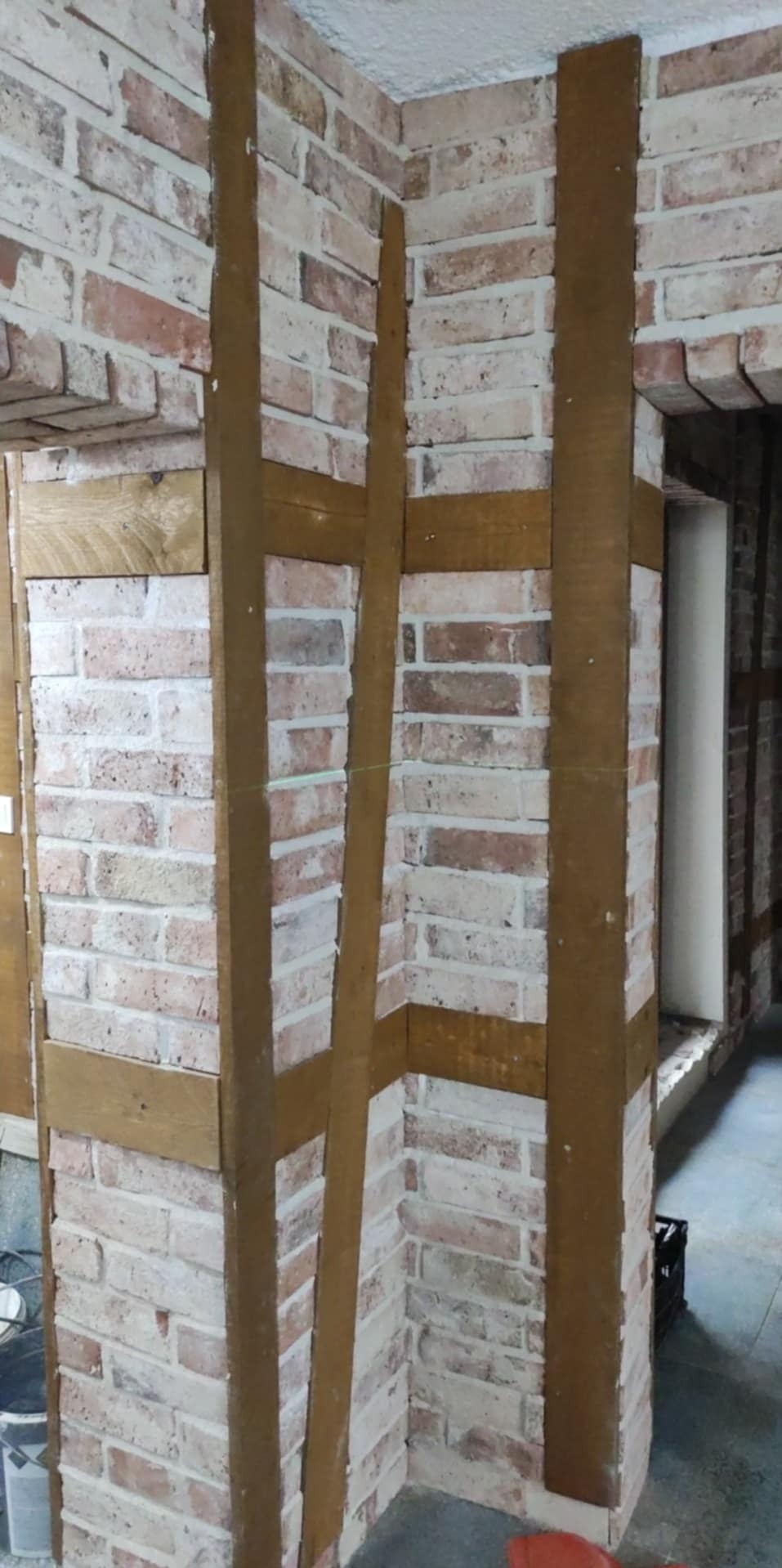 Wykończenie ściany imitacją cegły z drewnianymi elementami dekoracyjnymi. Widoczne fragmenty ściany i narożnika, prace w toku, surowy stan wykończenia.