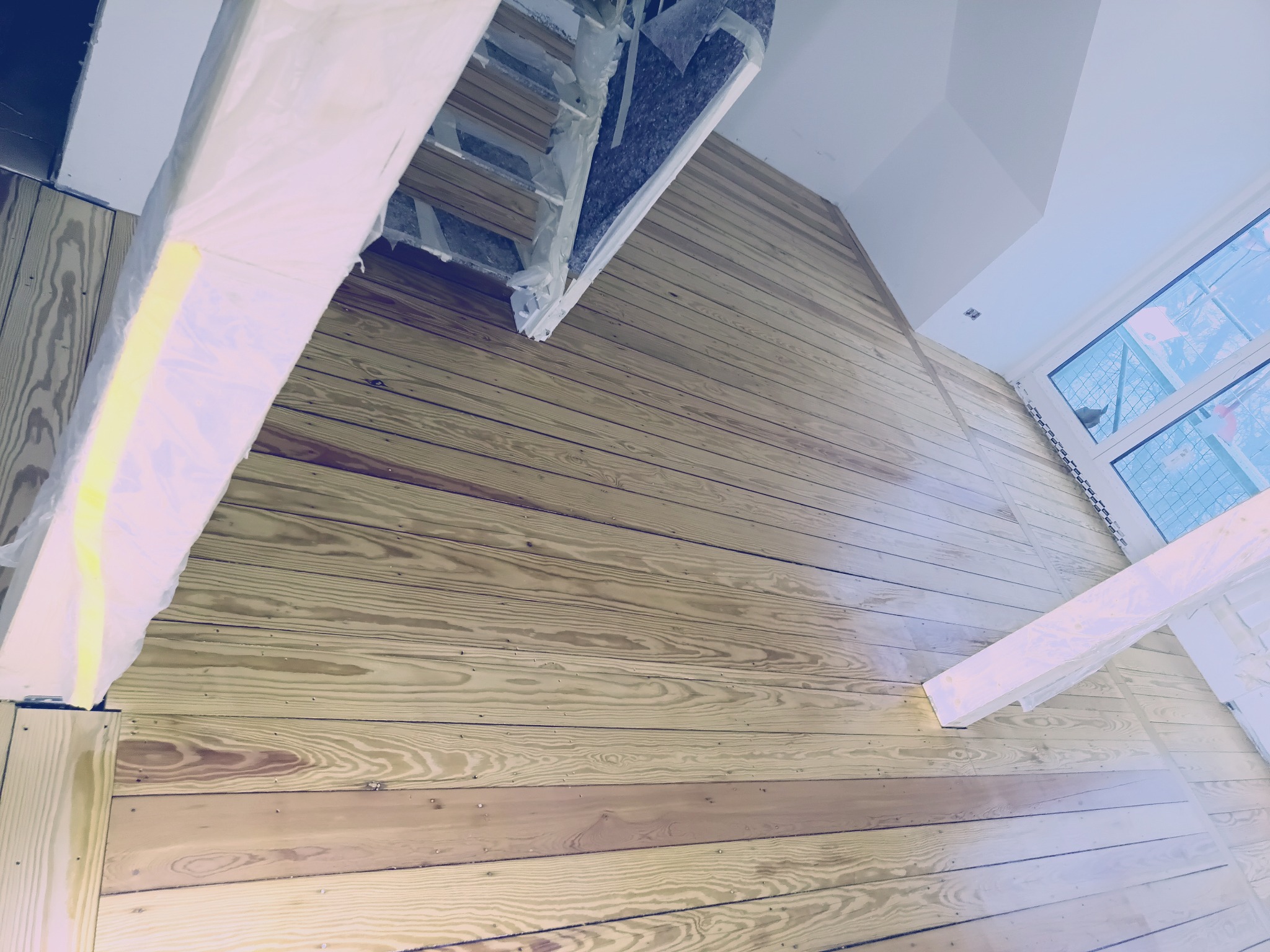 Ściana i sufit wykończone jasnym drewnem, widoczne okno i elementy konstrukcyjne zabezpieczone folią. Ukośne ujęcie podkreśla fakturę drewna i jasne wnętrze.