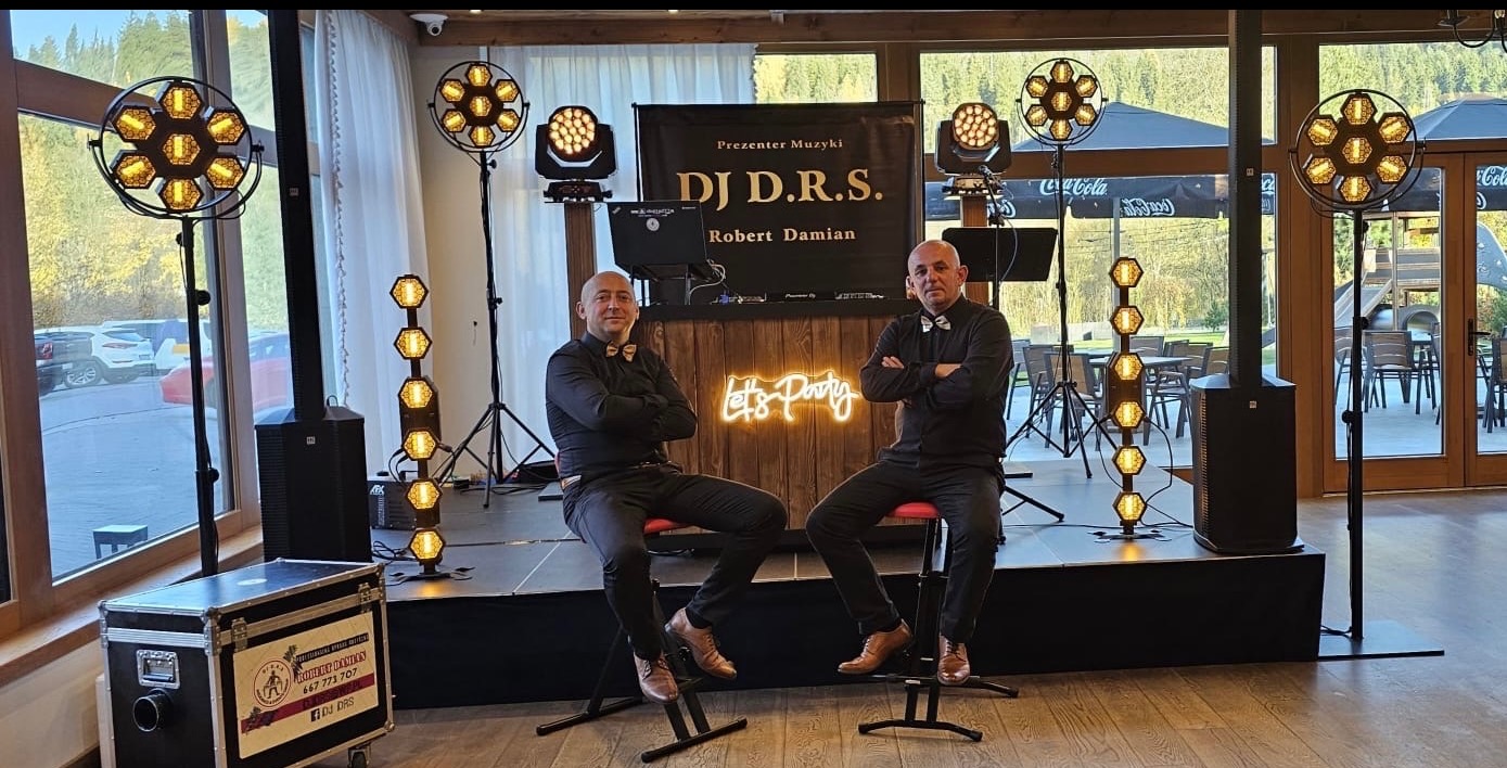 Zespół muzyczny DJ D.R.S. na scenie z oświetleniem eventowym. Dwóch muzyków siedzi na krzesłach barowych. Widoczny neon 'Let's Party' i sprzęt nagłośnieniowy.