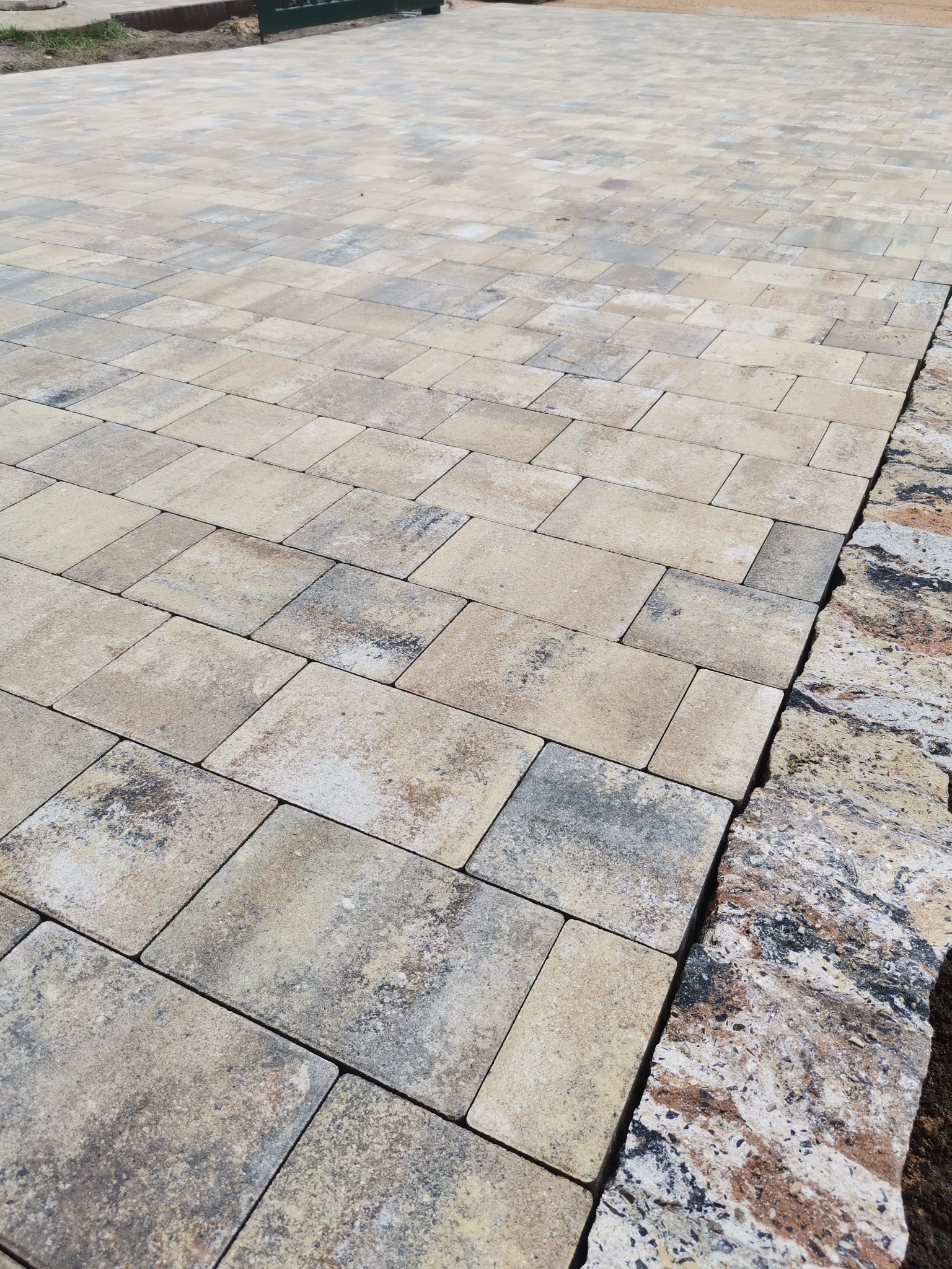 Ułożona kostka brukowa w odcieniach beżu i szarości, widoczna z perspektywy ukośnej, z fragmentem obrzeża z kamienia naturalnego po prawej stronie.