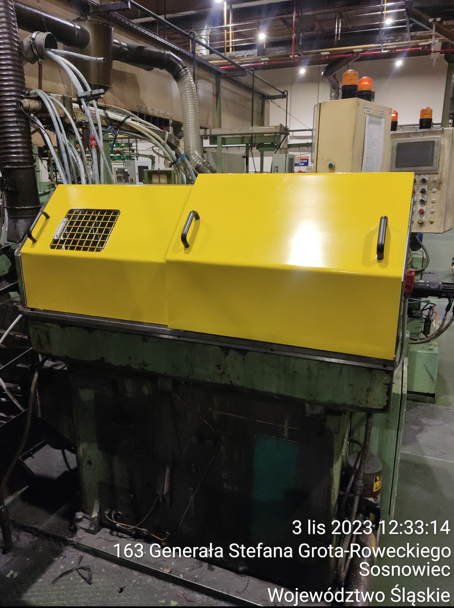 Żółta obudowa ochronna na maszynie przemysłowej, widoczne uchwyty i kratka wentylacyjna. W tle instalacje i elementy sterujące. Obudowa po renowacji.