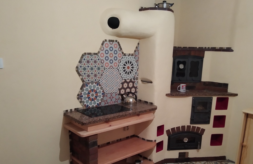 Unikatowy piec kaflowy z płytkami heksagonalnymi w marokańskim stylu, z płytą grzewczą i piekarnikiem. Na blacie czajnik i garnek.