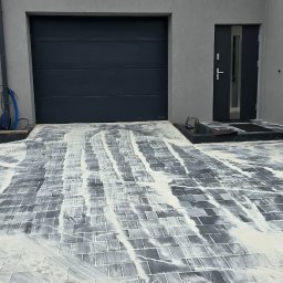 AD-Bruk - Nowoczesny podjazd z szarej kostki brukowej, świeżo po fugowaniu piaskiem kwarcowym, na tle domu z garażem i drzwiami wejściowymi. Widoczne ślady po pracy.