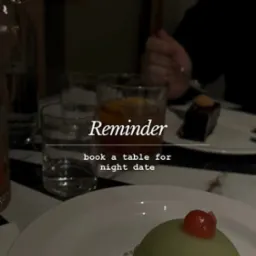 Deser z wisienką i czekoladowe ciastko na talerzu, szklanki z napojami i tekst 'Reminder book a table for night date' w ciemnej restauracji.
