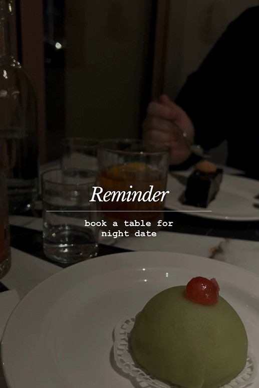 Deser z wisienką i czekoladowe ciastko na talerzu, szklanki z napojami i tekst 'Reminder book a table for night date' w ciemnej restauracji.