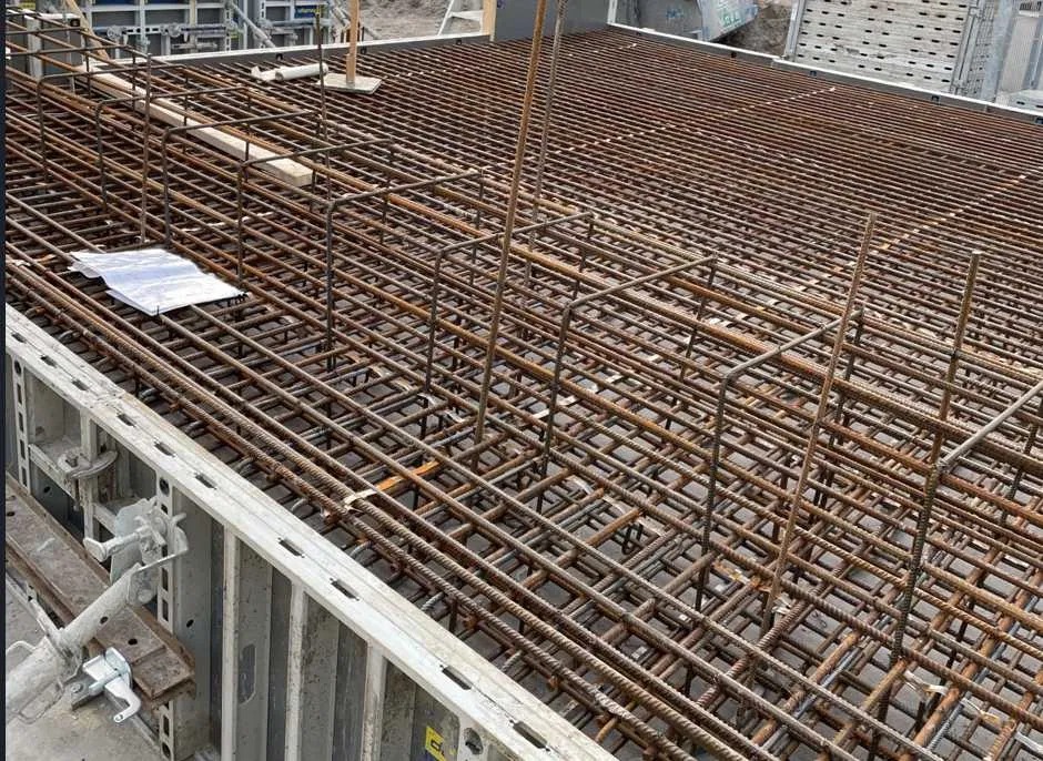 Zbrojenie fundamentu z metalowych prętów, widoczne szalunki. Konstrukcja przygotowana do zalania betonem, z bliska, z góry.