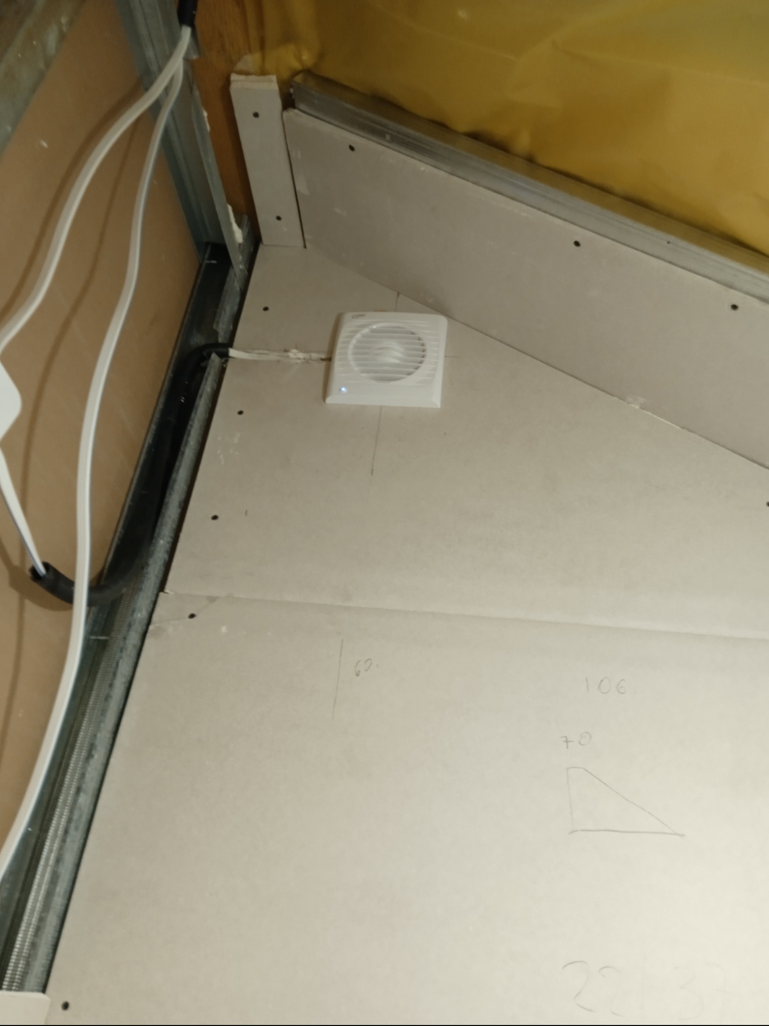 Skośne poddasze z płytami karton-gips, widoczny wentylator, metalowe profile, instalacja elektryczna i izolacja. Na płytach widoczne odręczne notatki.