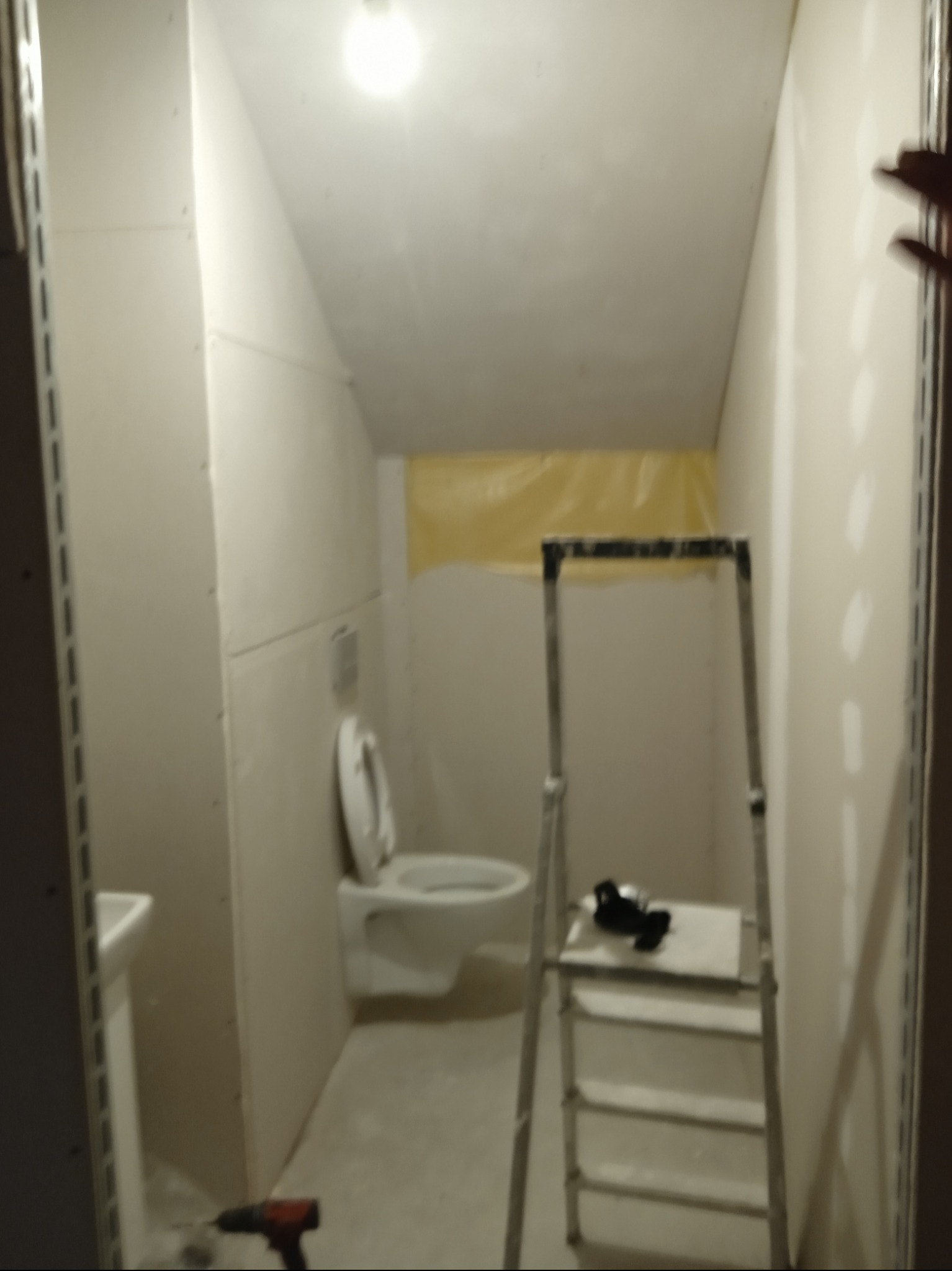 Montaż płyt karton-gips w łazience na poddaszu. Widoczna toaleta, drabina, narzędzia i częściowo zamontowane płyty G-K.