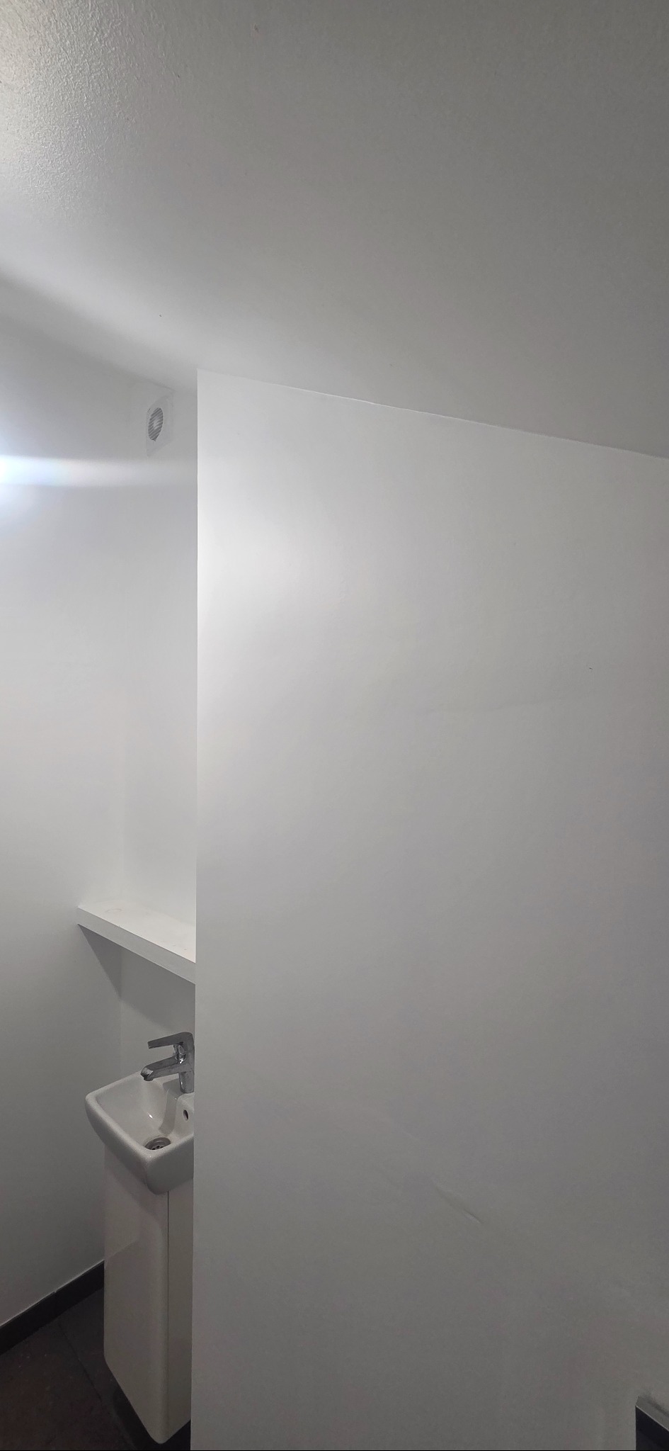 Białe wnętrze łazienki z umywalką na postumencie, widoczne gładzie na ścianach i sufit z oświetleniem punktowym. Minimalistyczny design w jasnej tonacji.