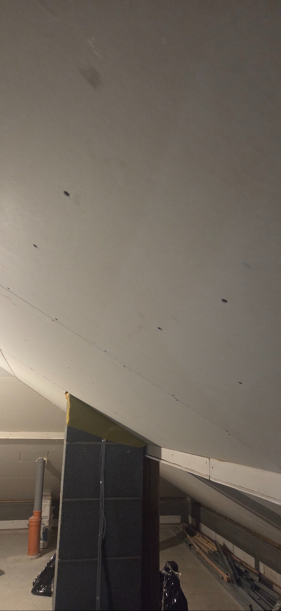 Poddasze po montażu płyt kartonowo-gipsowych, widoczne łączenia płyt i izolacja. Elementy instalacji w tle. Ukończony etap prac wykończeniowych.