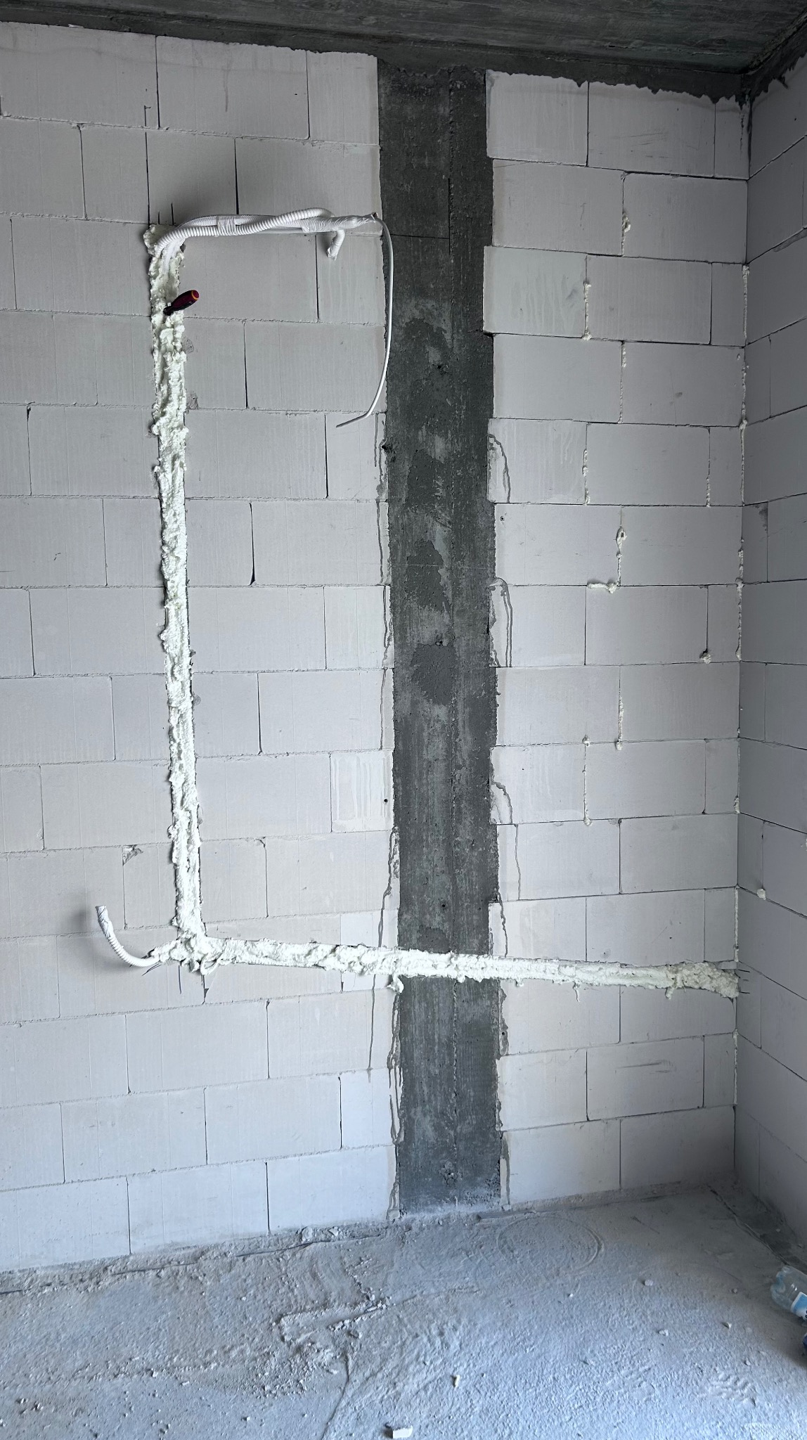 Ściana z betonu komórkowego z wyciętymi bruzdami na instalację, wypełnionymi pianką montażową. Widoczny przewód instalacyjny. Pionowa bruzda zalana betonem.