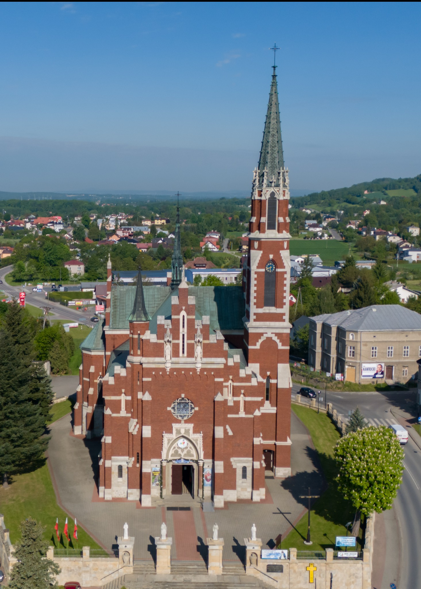 Panorama kościoła z cegły z wysoką wieżą i iglicą na tle zielonego krajobrazu miejskiego w słoneczny dzień. Widok z góry.