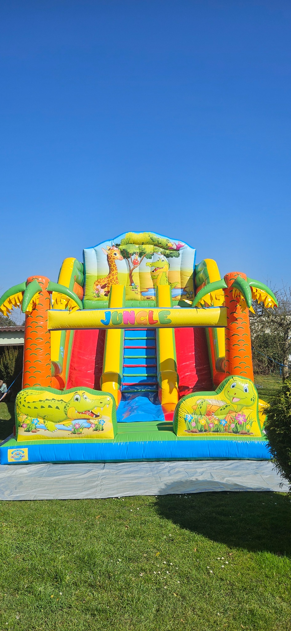 Kolorowy, dmuchany plac zabaw w stylu dżungli z żyrafą i krokodylami, rozstawiony na trawie w Rydułtowach, pod błękitnym niebem. Atrakcja na imprezę.