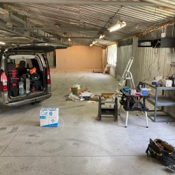 MVP Marian Olejnik - Instalacja kabli CAT6 w garażu: otwarty bagażnik auta z narzędziami, drabina, stół roboczy z akcesoriami, skrzynka kabli. Widoczne okablowanie przy ścianie.