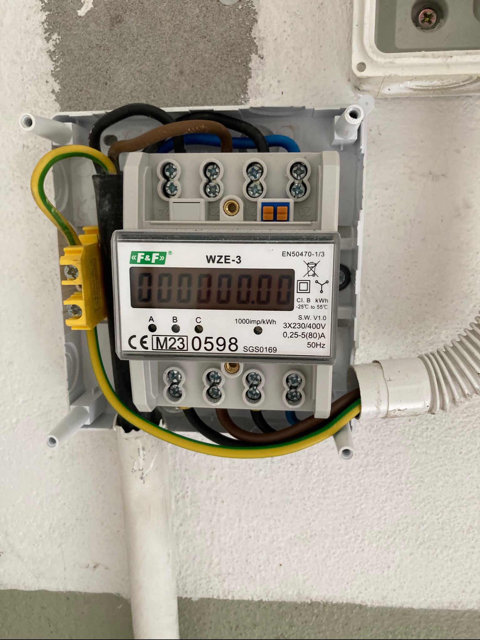 Zamontowany licznik energii elektrycznej WZE-3 marki F&F w białej obudowie, z widocznymi przewodami i złączkami. Szczegółowy widok na instalację elektryczną.