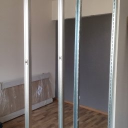 Zielony Fundament - Montaż metalowej konstrukcji szkieletowej do ścianki działowej z płyty karton-gips w jasnym wnętrzu. Widoczne narzędzia i fragmenty podłogi.