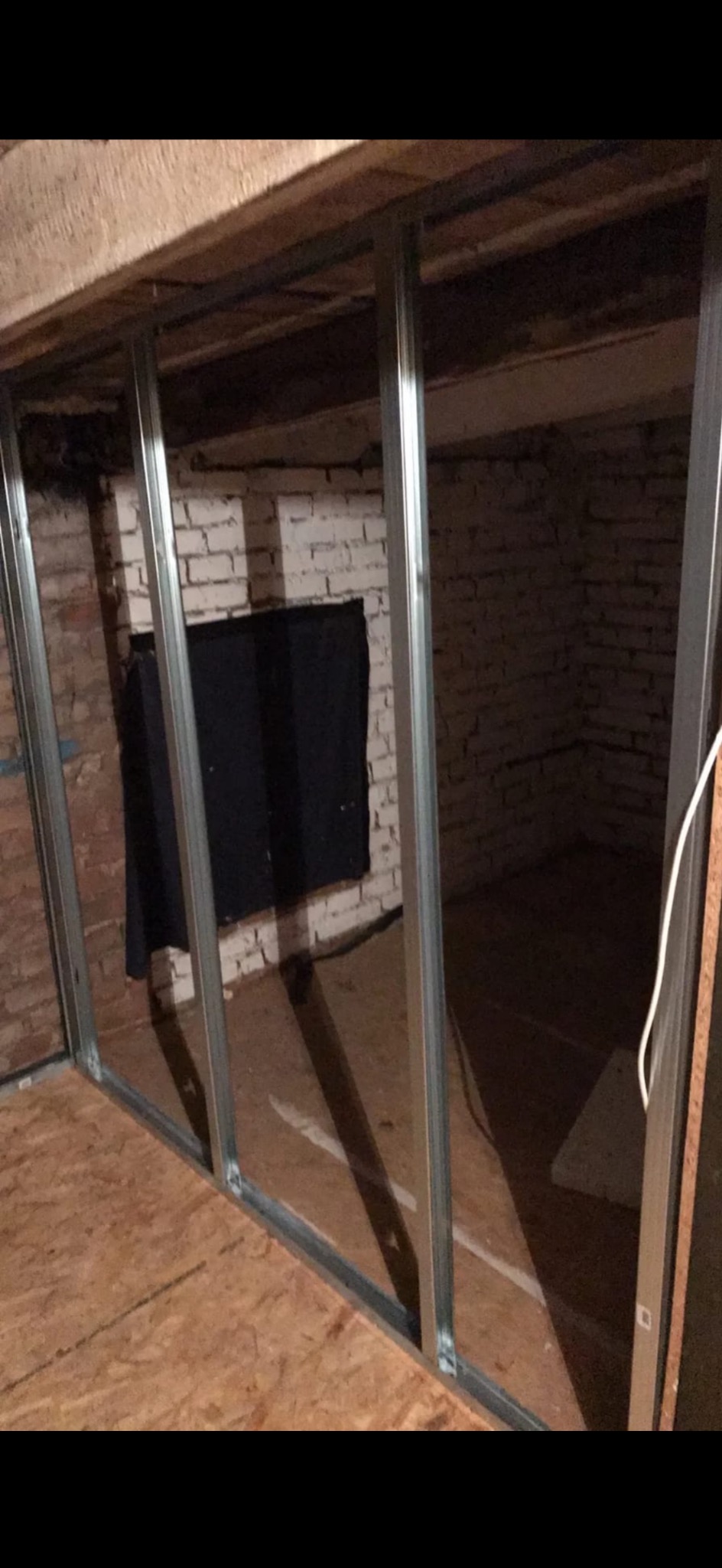 Montaż metalowego stelaża na poddaszu z widoczną starą cegłą i płytą OSB na podłodze. Stelaż przygotowany pod płyty gipsowe.