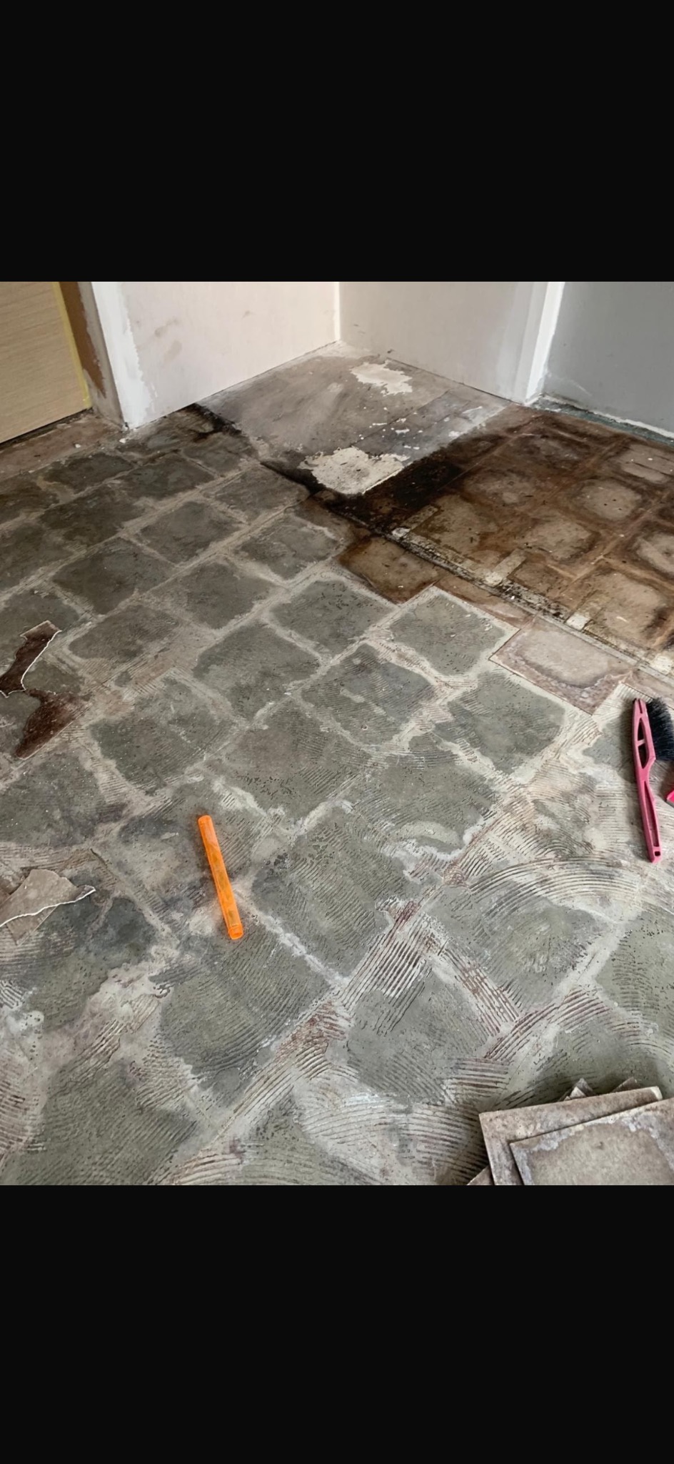 Przygotowanie podłoża pod płytki: resztki kleju i starej posadzki. Widoczne narzędzia i fragmenty płytek. Podłoże z charakterystycznym wzorem.