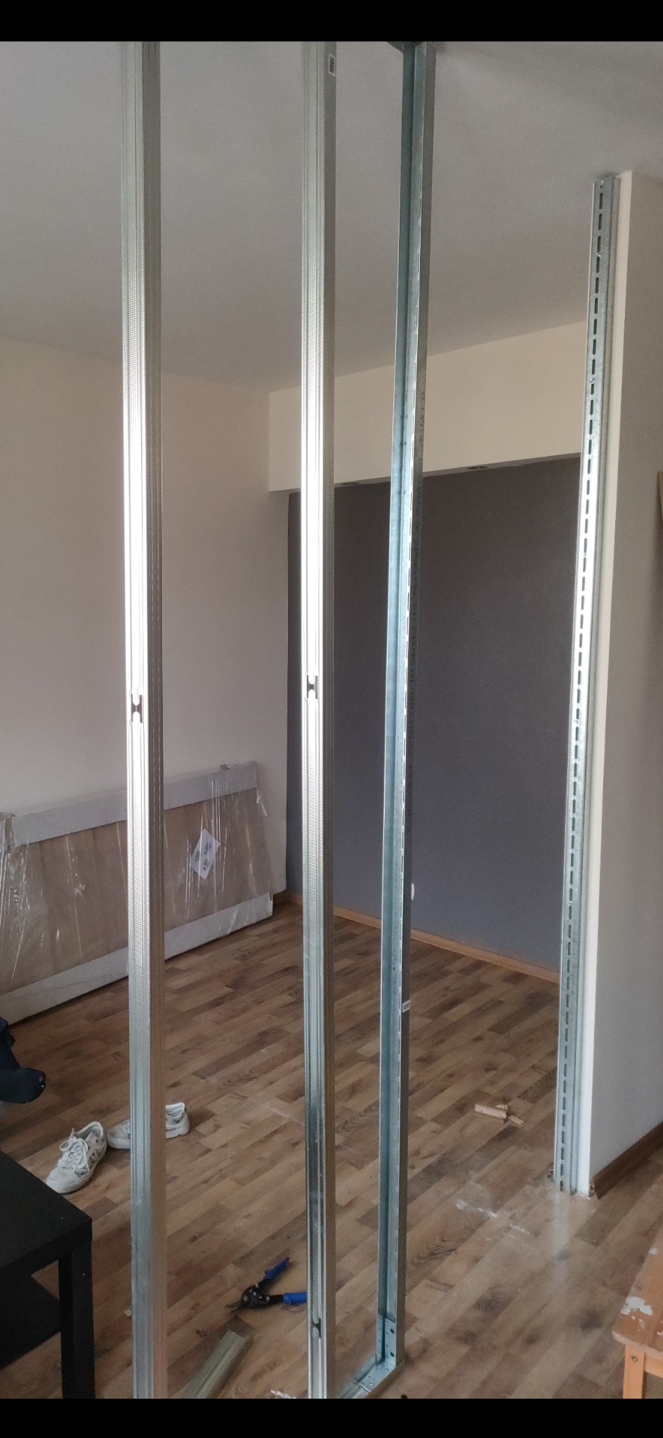 Montaż metalowej konstrukcji szkieletowej do ścianki działowej z płyty karton-gips w jasnym wnętrzu. Widoczne narzędzia i fragmenty podłogi.