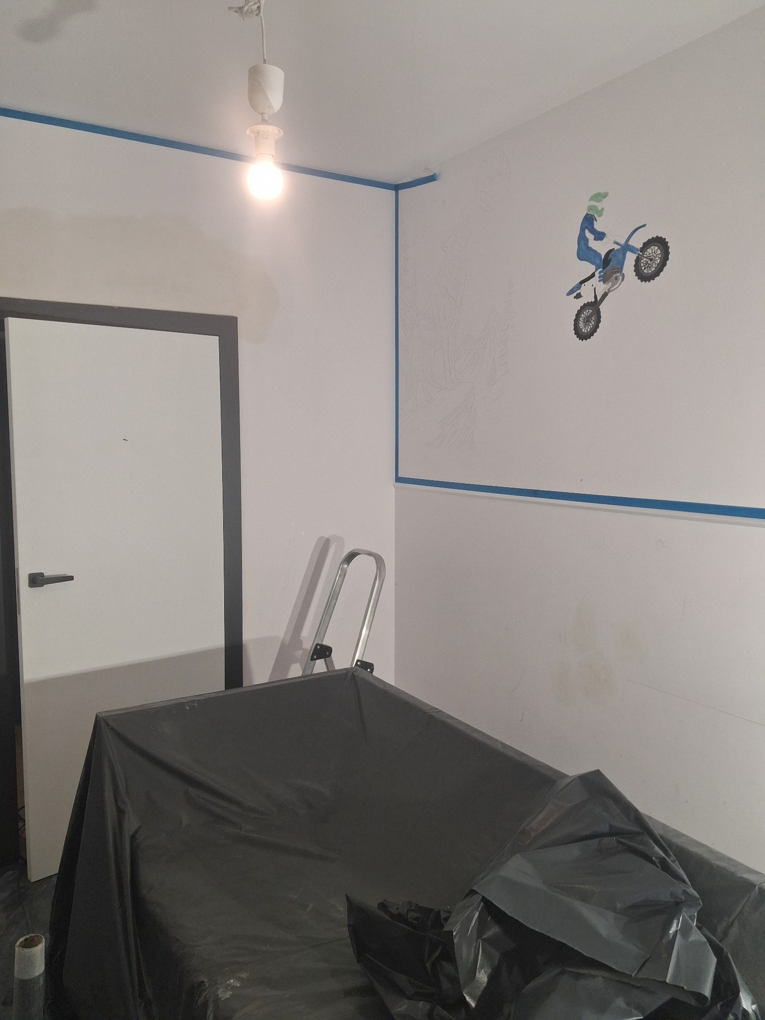Pokój w trakcie malowania z motywem motocyklisty na ścianie. Zabezpieczone meble folią, widoczna drabina i taśma malarska. Etap prac wykończeniowych.