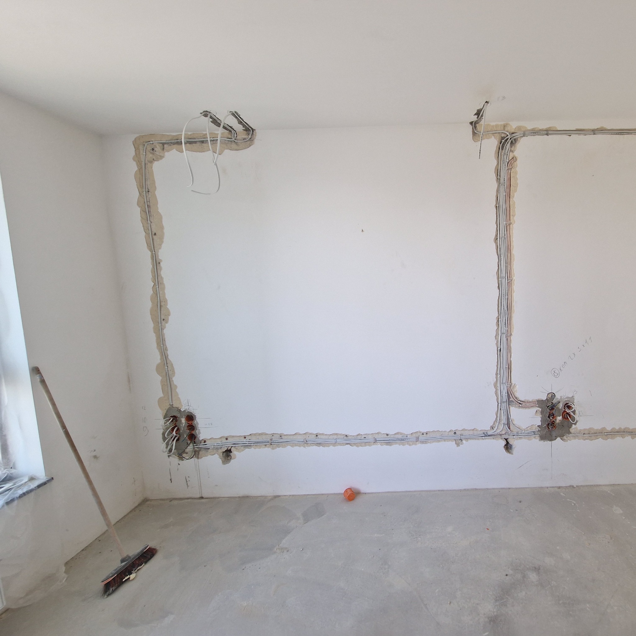 Ściana w trakcie montażu instalacji elektrycznej. Widoczne kable w bruzdach, puszki pod gniazdka, narzędzia. Surowy stan, przygotowanie do dalszych prac wykończeniowych.