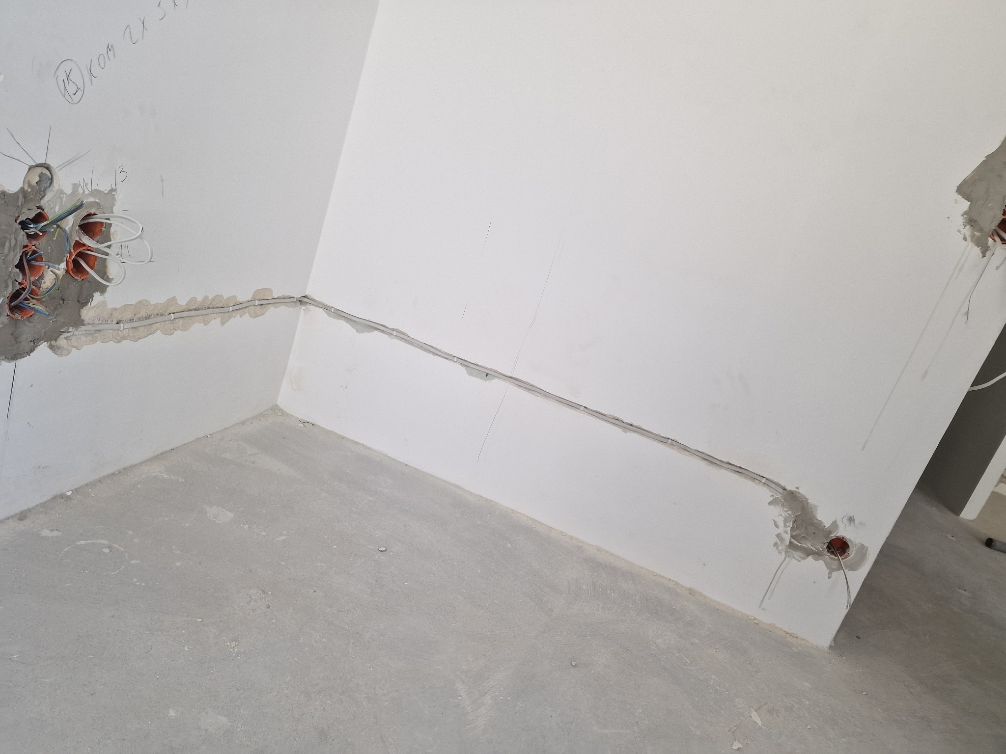 Fragment wnętrza w trakcie prac elektrycznych: widoczne kable w ścianach, puszki instalacyjne i surowe wykończenie ścian. Etap prac przed tynkowaniem.