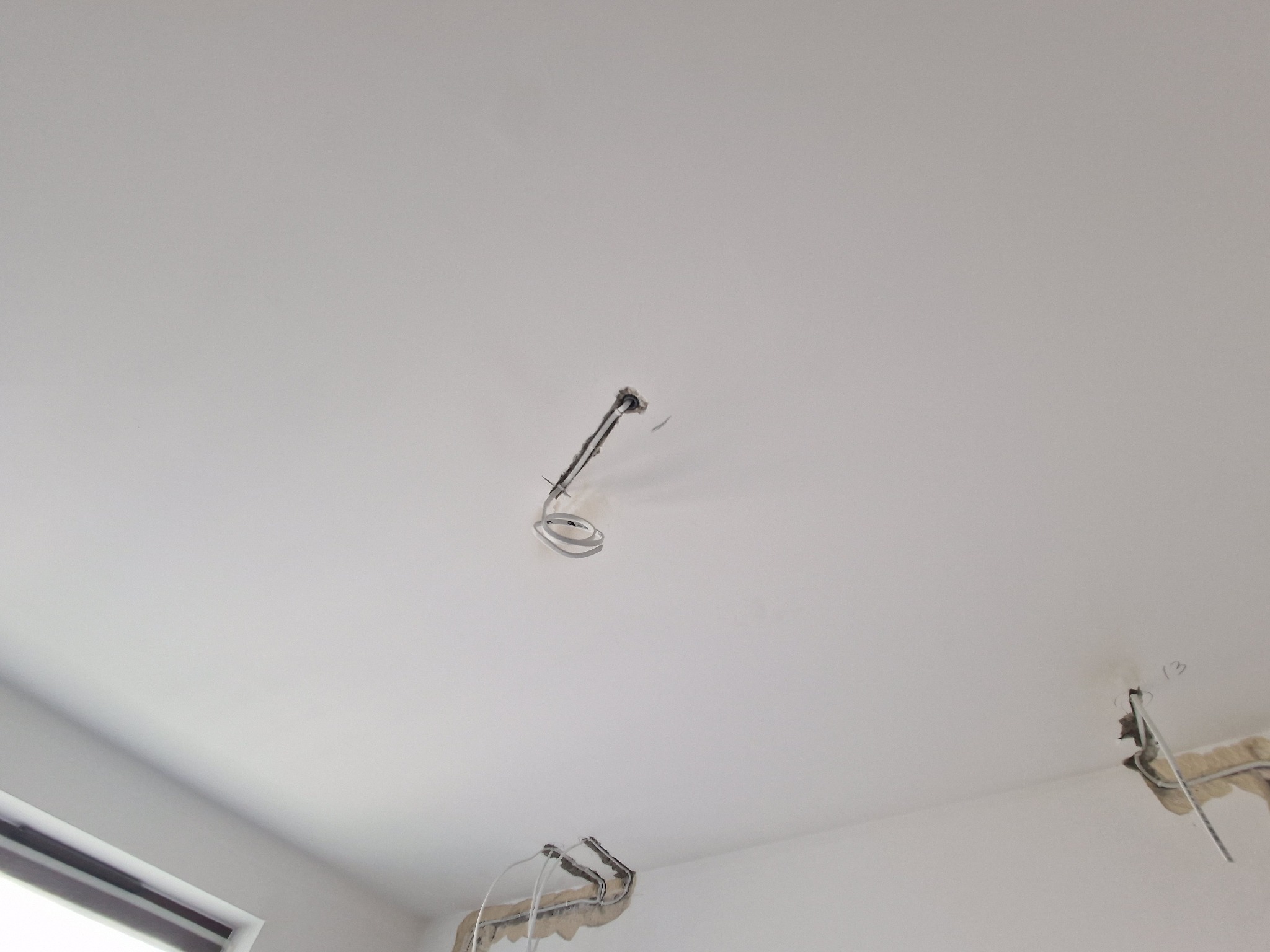 Biały sufit z trzema otworami, z których wystają przewody elektryczne, widoczne ślady po kuciu, przygotowanie do montażu oświetlenia.