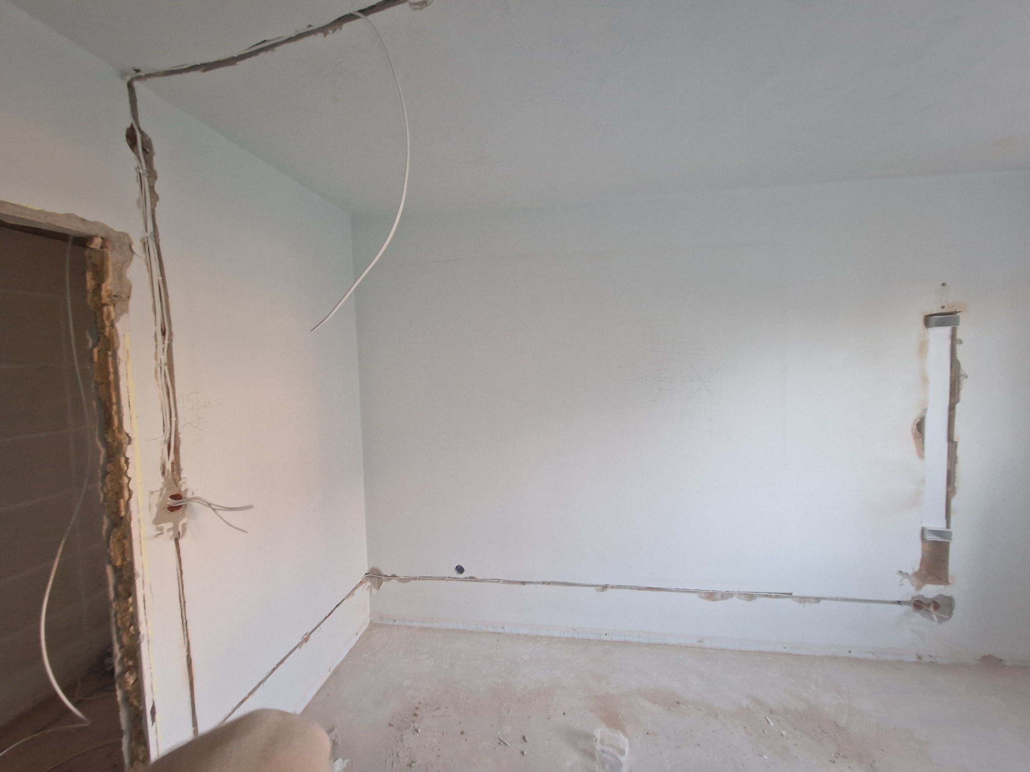 Białe wnętrze w trakcie prac elektrycznych: kable prowadzone w ścianach i pod sufitem, widoczne puszki. Przygotowanie do wykończenia, surowy stan.