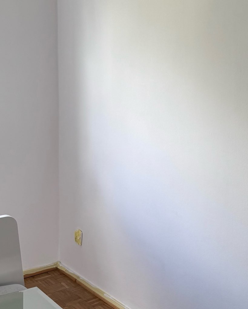 Ściana po malowaniu z zabezpieczonymi listwami przypodłogowymi taśmą malarską i zaklejonym gniazdkiem. Parkiet w jodełkę.