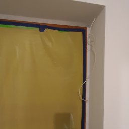 Mykola Iskovych - Zabezpieczona folią i taśmą ściana przed malowaniem, widoczny narożnik sufitu i fragment ściany. Ochrona przed zabrudzeniem farbą.