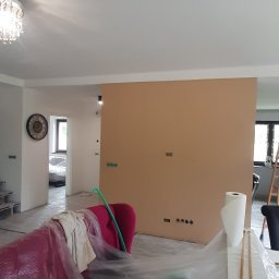 Mykola Iskovych - Przygotowania do malowania ścian w Jankowicach. Zabezpieczone meble folią malarską, ściana w kolorze beżowym, widoczne gniazdka elektryczne i listwy przypodłogowe.