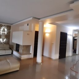 Mykola Iskovych - Przestronny salon po renowacji z beżowymi ścianami, kominkiem obłożonym kamieniem i błyszczącą podłogą. Widoczne kolumny i nowoczesne oświetlenie.