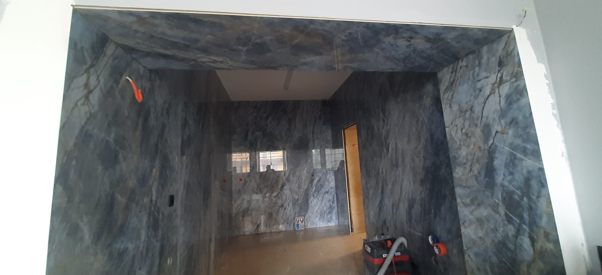 Łazienka w trakcie wykańczania z marmurową okładziną ścian i sufitu. Widoczne narzędzia i instalacje elektryczne. W tle okno.