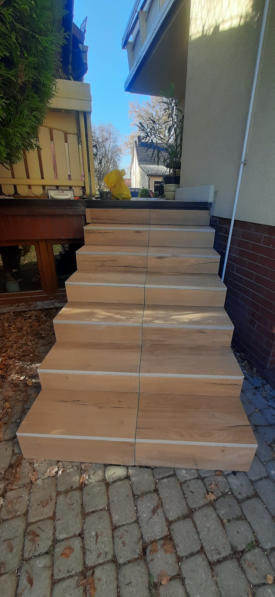 Wykończone schody zewnętrzne z płytek imitujących drewno, z widocznymi fugami i detalami wykończeniowymi. Ujęcie z dołu, podkreślające solidność i estetykę wykonania.