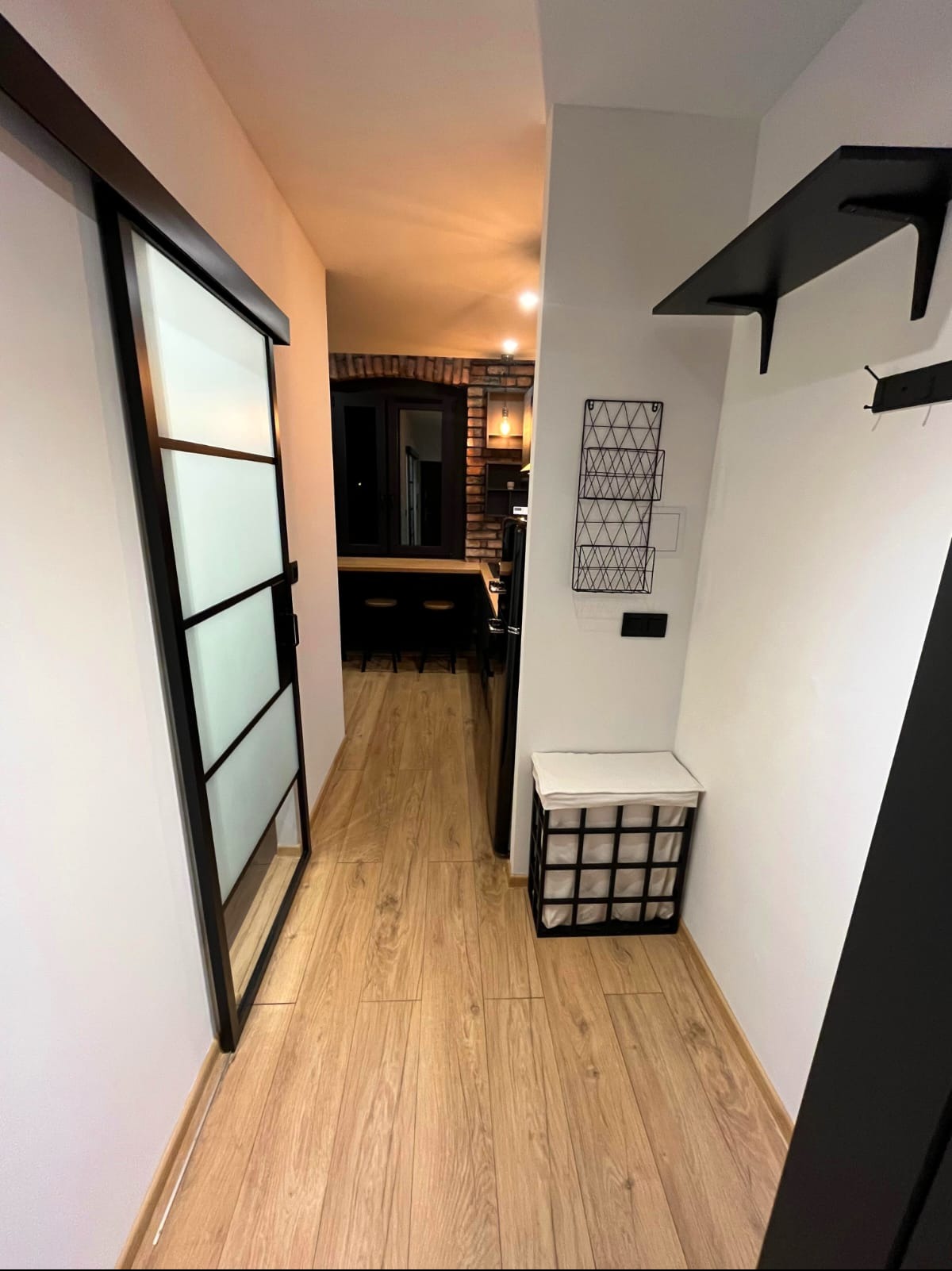 Nowoczesne wnętrze: przesuwne drzwi z czarną ramą, drewniana podłoga, ceglana ściana w tle. Minimalistyczny design z elementami loftu.