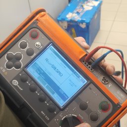 Usługi hydrauliczno-budowlane Adrian Bugała - Pomiar rezystancji izolacji miernikiem Sonel MPI-520. Na ekranie wynik Riso=59,5MΩ. Widoczne przewody pomiarowe i dłoń osoby wykonującej pomiar.