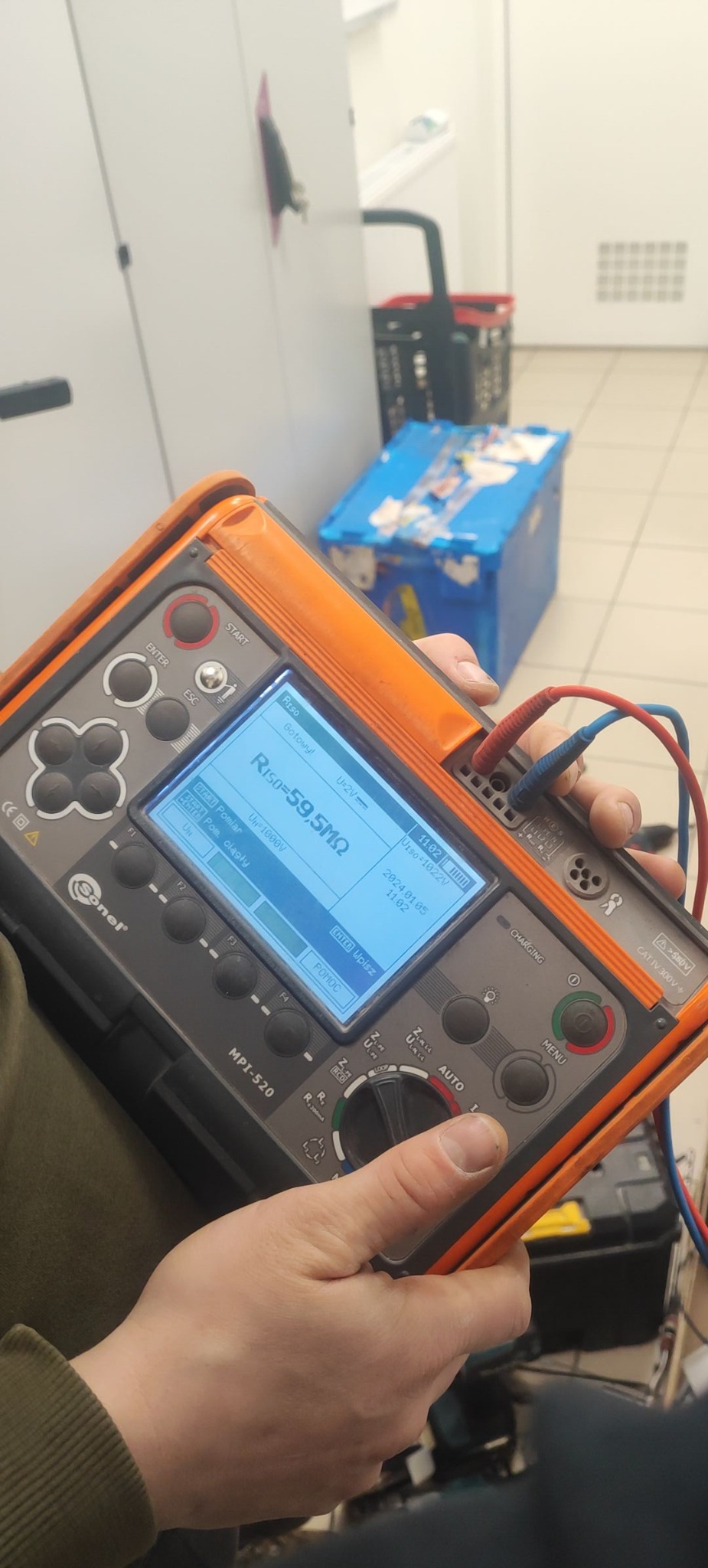 Pomiar rezystancji izolacji miernikiem Sonel MPI-520. Na ekranie wynik Riso=59,5MΩ. Widoczne przewody pomiarowe i dłoń osoby wykonującej pomiar.