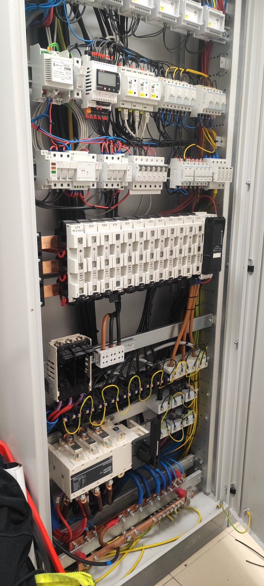 Rozdzielnia elektryczna w szafie, widoczne bezpieczniki, kable i szyny zbiorcze. Instalacja po montażu, gotowa do pracy.