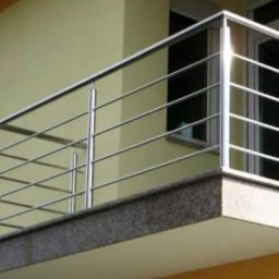 ProSteel - Nowoczesna balustrada balkonowa ze stali nierdzewnej z szarym kamiennym wykończeniem, widok z dołu, jasne tło budynku.