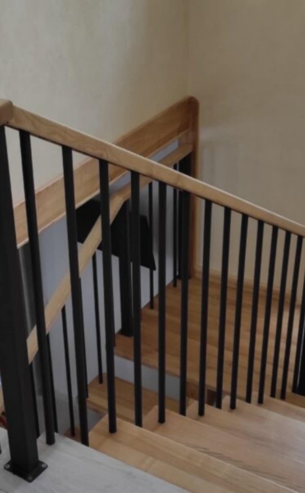Jasne drewniane schody z czarnymi, pionowymi prętami balustrady i drewnianym poręczem, widziane z dołu pod kątem. Minimalistyczny design.
