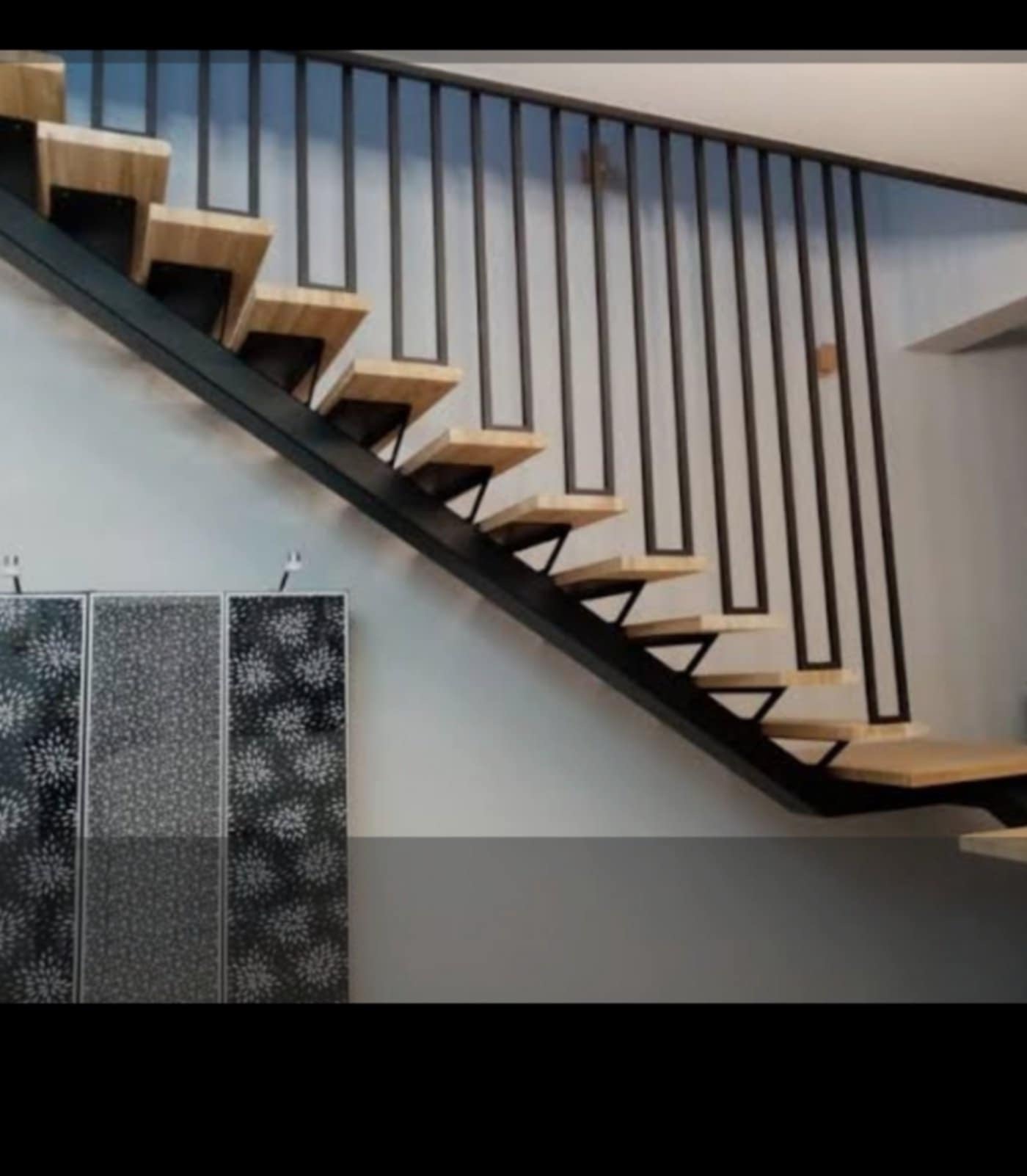 Nowoczesne schody z drewnianymi stopniami i czarną metalową balustradą o minimalistycznym designie. Widok z boku, w tle ściana i dekoracyjny panel.