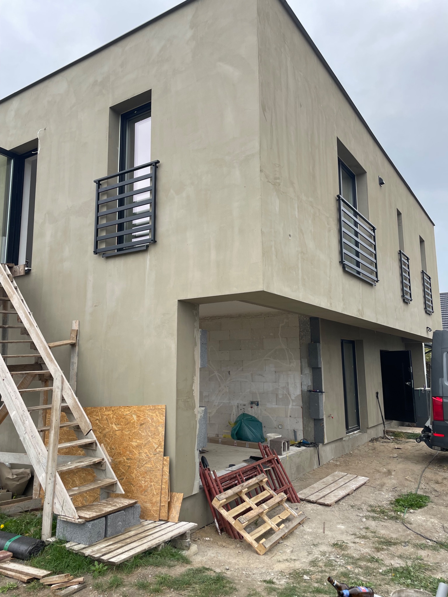 Nowoczesny dom w trakcie wykończenia z czarnymi, minimalistycznymi balustradami okiennymi. Widoczne rusztowania i materiały budowlane.