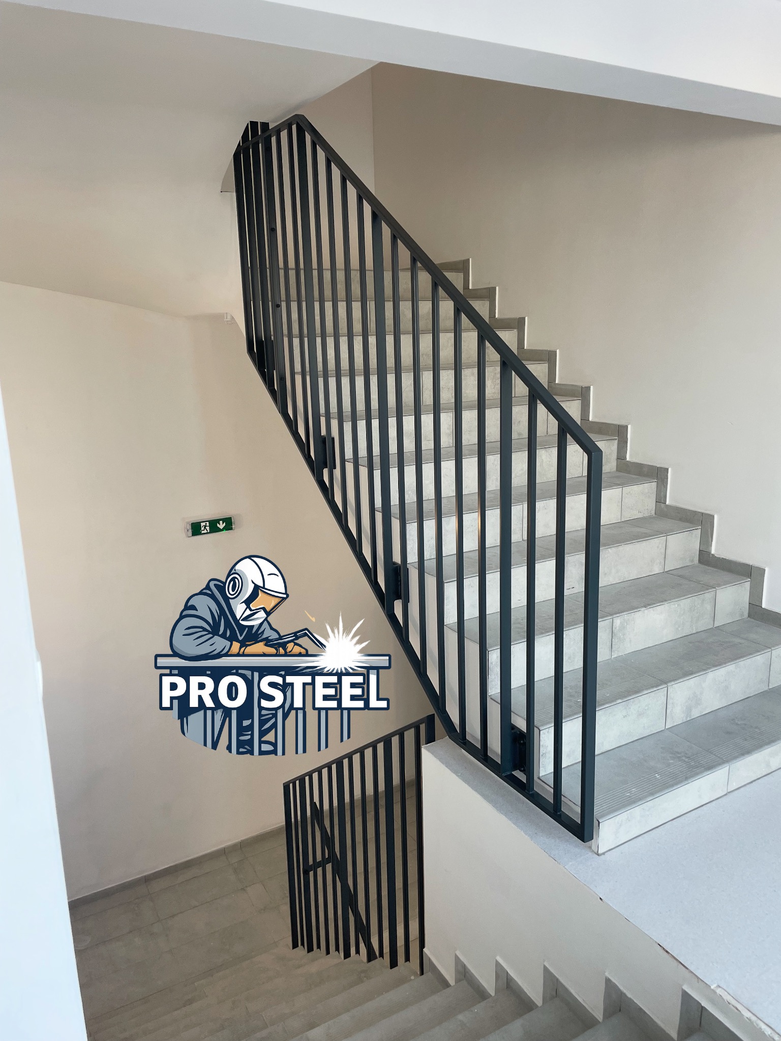 Nowoczesna, czarna balustrada schodowa z pionowymi szczeblami, zamontowana wewnątrz budynku. Widok z dołu na jasne schody i ścianę z logo firmy.