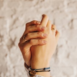 Daria Kriger Photography - Złączone dłonie z pierścionkami i bransoletkami na tle białej ściany z cegieł. Dłoń z bransoletką z zawieszką w kształcie serca.