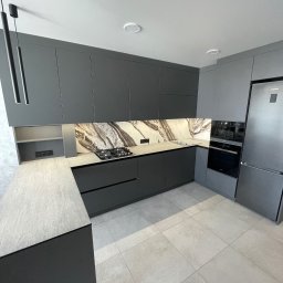 TTM - Nowoczesna, szara kuchnia z marmurowym backsplashiem i oświetleniem LED. Minimalistyczny design z frontami bez uchwytów i sprzętem AGD w zabudowie.