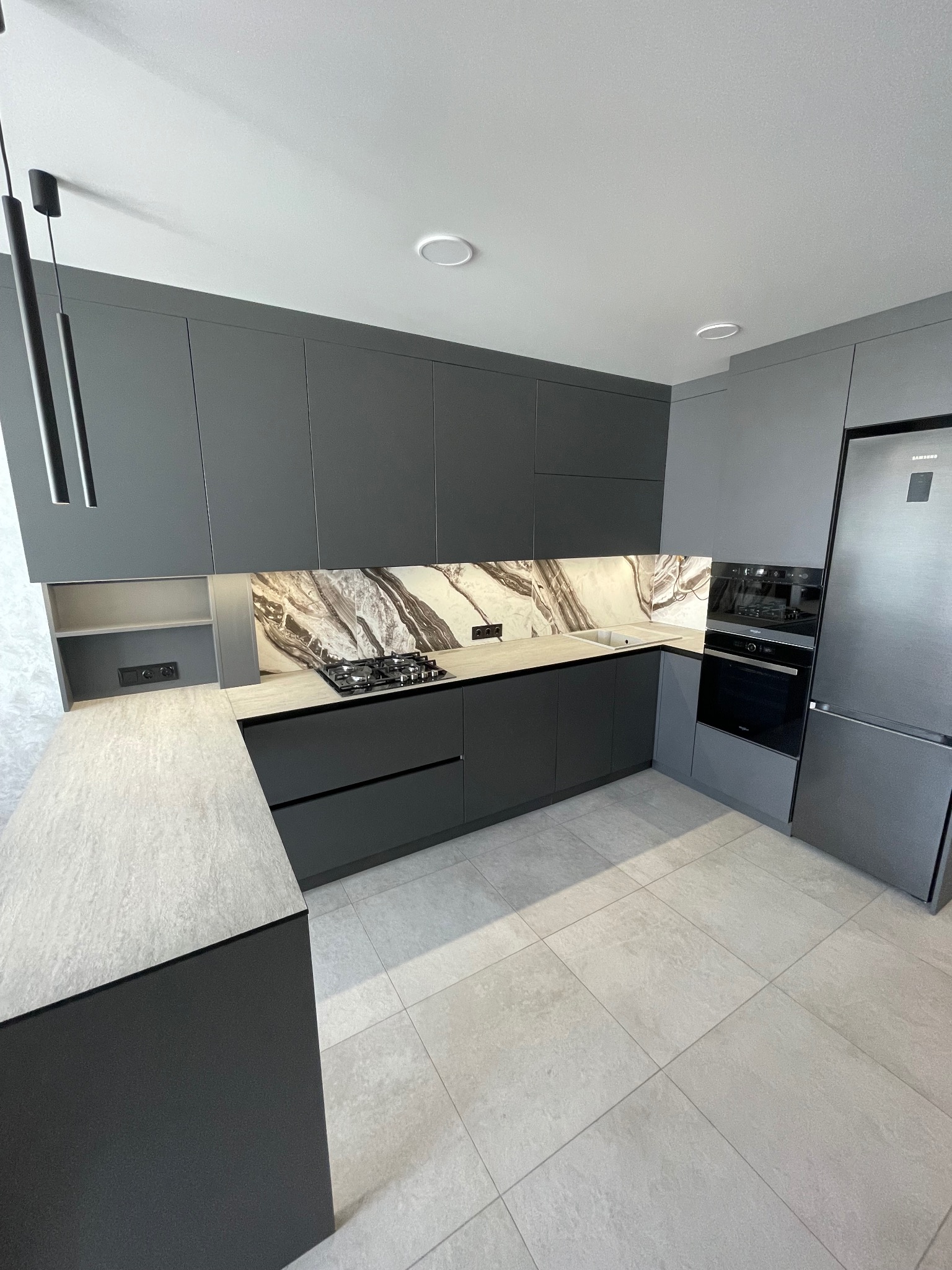 Nowoczesna, szara kuchnia z marmurowym backsplashiem i oświetleniem LED. Minimalistyczny design z frontami bez uchwytów i sprzętem AGD w zabudowie.
