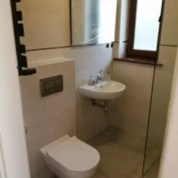 Nowoczesna, jasna łazienka po remoncie: beżowe płytki, podwieszana toaleta, umywalka na ścianie, grzejnik drabinkowy i lustro z oświetleniem. Minimalistyczny design.