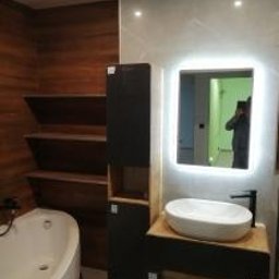 Katarzyna - Nowoczesna łazienka z wanną, umywalką na szafce, lustrem z podświetleniem LED i drewnianymi półkami. Minimalistyczny design z akcentem drewna.