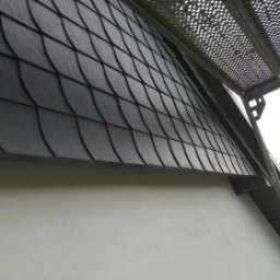 Katarzyna - Elewacja domu z ciemną, łuskową okładziną, widoczna spod rusztowania. Świeżo pomalowana, biała ściana i fragment zieleni w tle. Ujęcie z dołu.