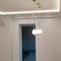 Katarzyna - Białe wnętrze po remoncie: dekoracyjne panele ścienne, podwieszany sufit z oświetleniem LED, wisząca lampa i obrazy z motywem liści. Wykończenie w stylu nowoczesnym.